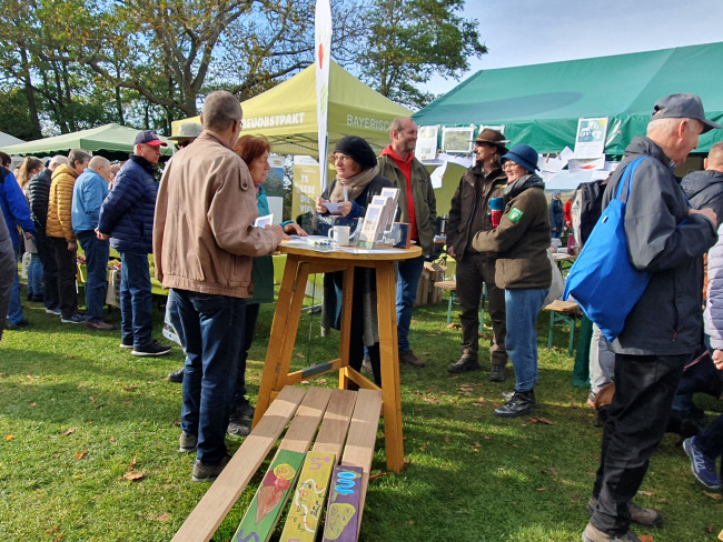 Menschen rund um einen Stehtisch und vor Pavillon